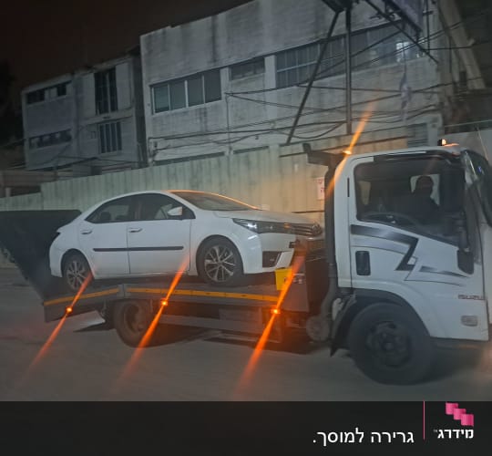 גרר עם רכב לבן על משאית גרירה בלילה